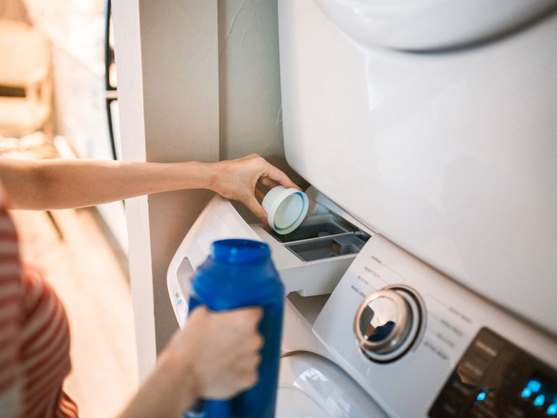 Personne versant de la lessive dans une machine à laver