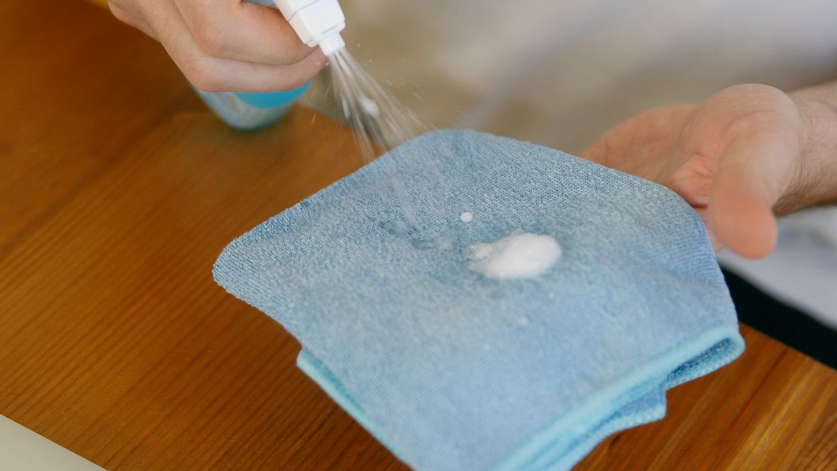 Chiffon microfibre bleu avec produit désinfectant posé sur un ordinateur portable