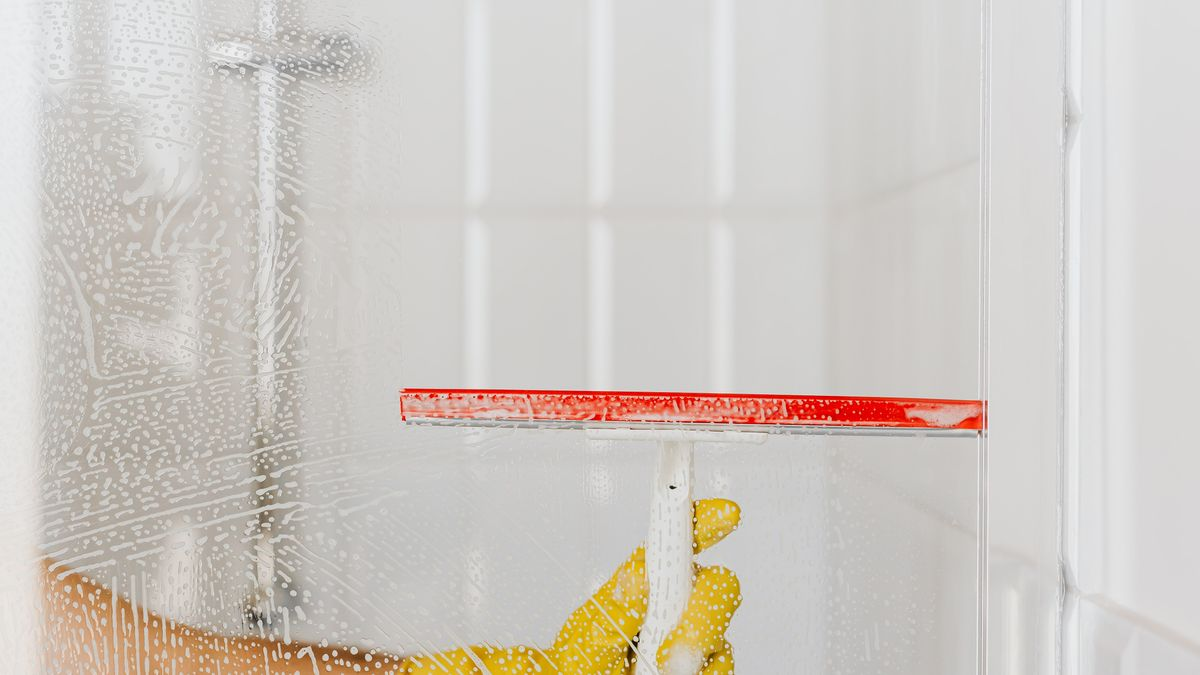Personne nettoyant une paroi de douche en verre couverte de calcaire