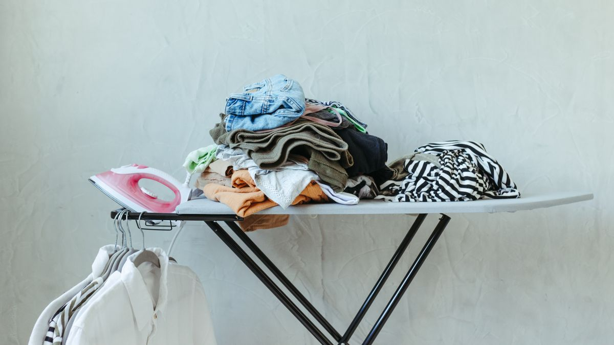 Pile de vêtements pliés sur une planche à repasser, chemises blanches suspendues à côté